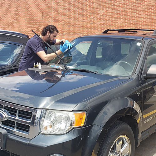 auto glass Burlington technician is repairing customer front windshield in the parking lot emergency mobile auto glass repair service by Speers Auto Glass